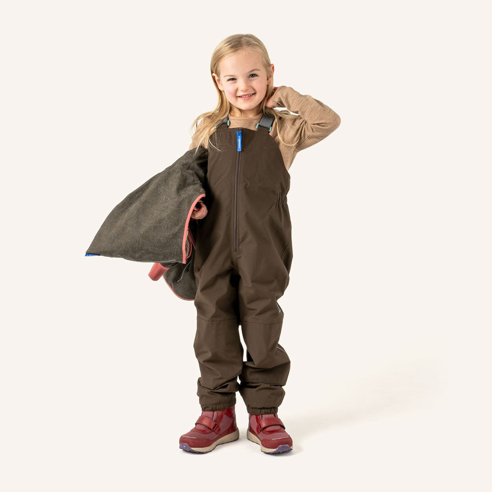 Kinder-Latzhose von PIKKU LATULI, dunkelbraun, mit Reißverschluss und Trägern am Modell