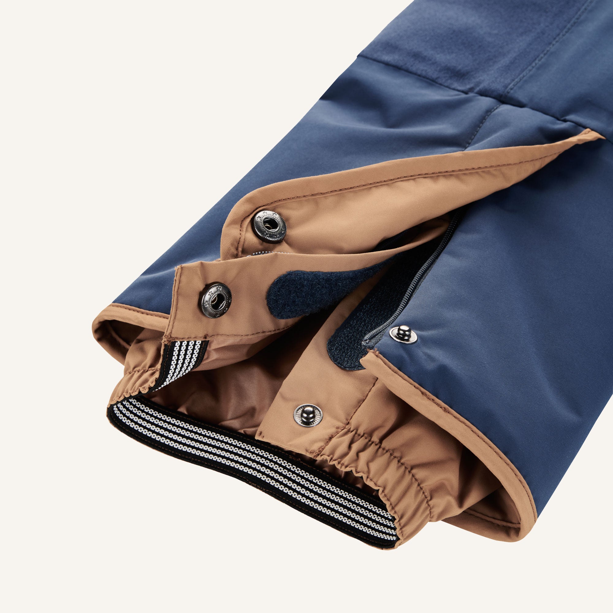 Snow pants detail: dark blue fabric with beige inner lining, snaps and zipper at the cuff